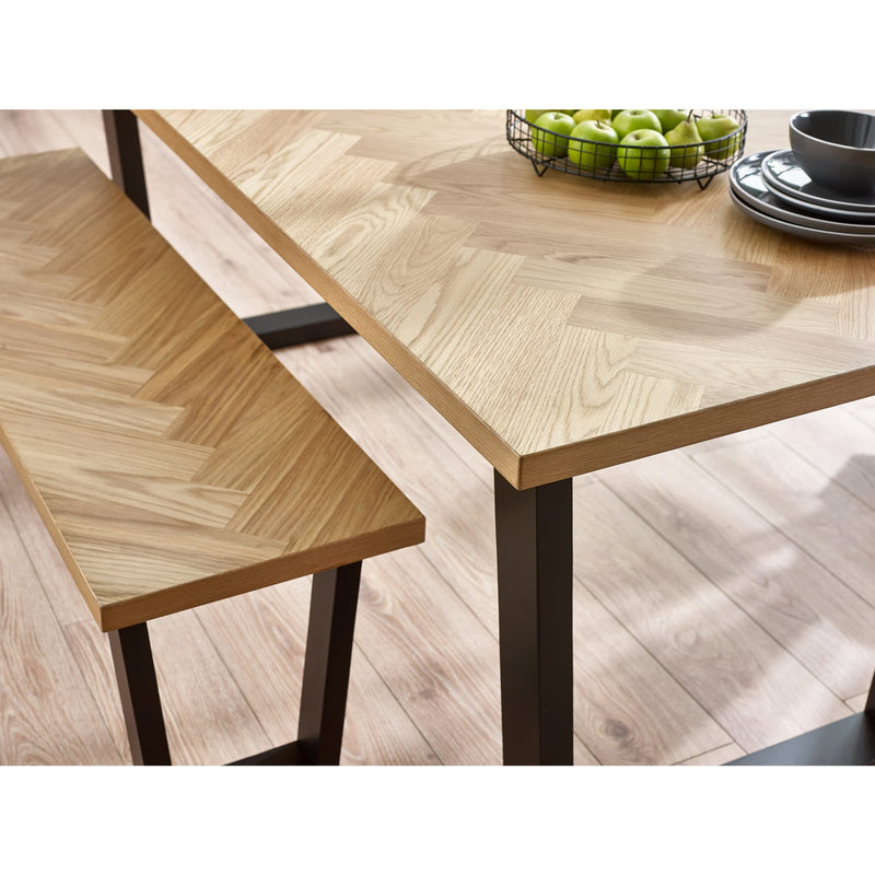 Wooden dining table with herringbone pattern and bench on a light wood floor.