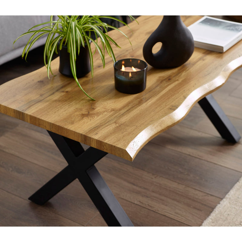 Wooden coffee table with black metal legs, candle, and plant in a living room setting.