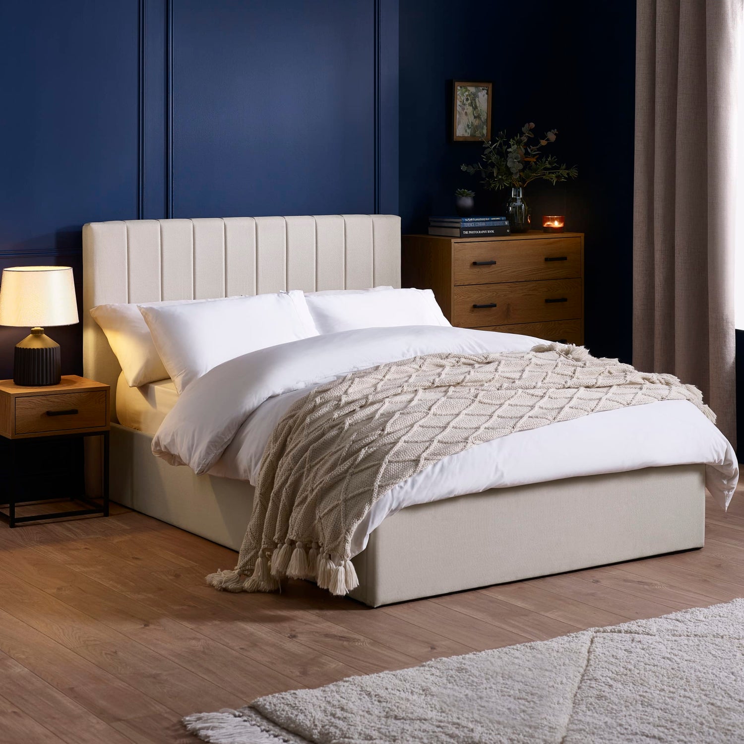 Neatly made bed with beige headboard and bedding in a bedroom setting.