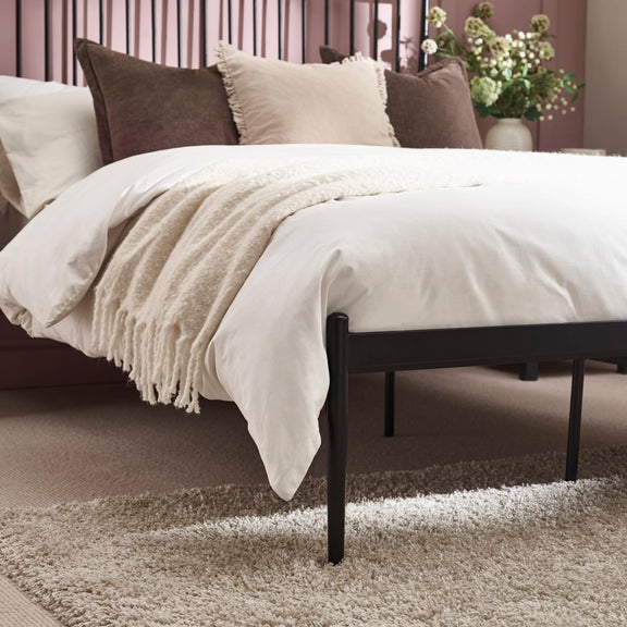 Bed with white bedding and brown and beige pillows on a carpeted floor.