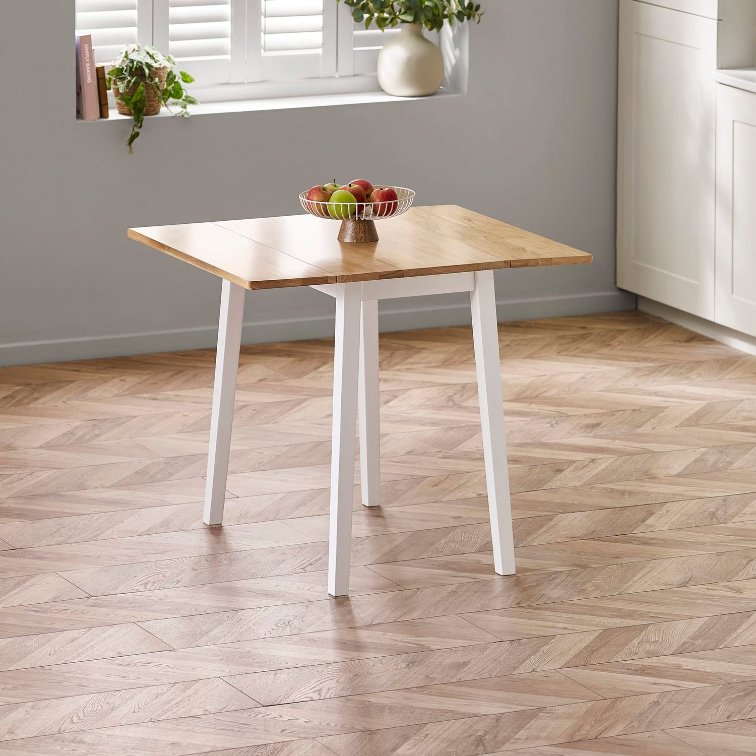 Wooden table with white legs on a wooden floor, near a window with plants.