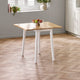Wooden table with white legs on a wooden floor, near a window with plants.