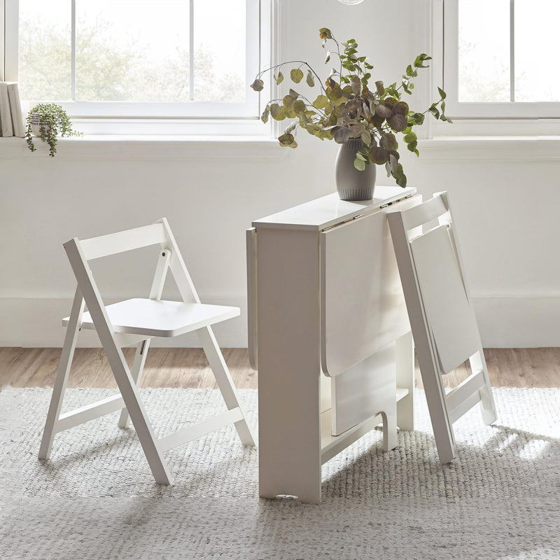 White folding table with two chairs in a bright room with large windows.