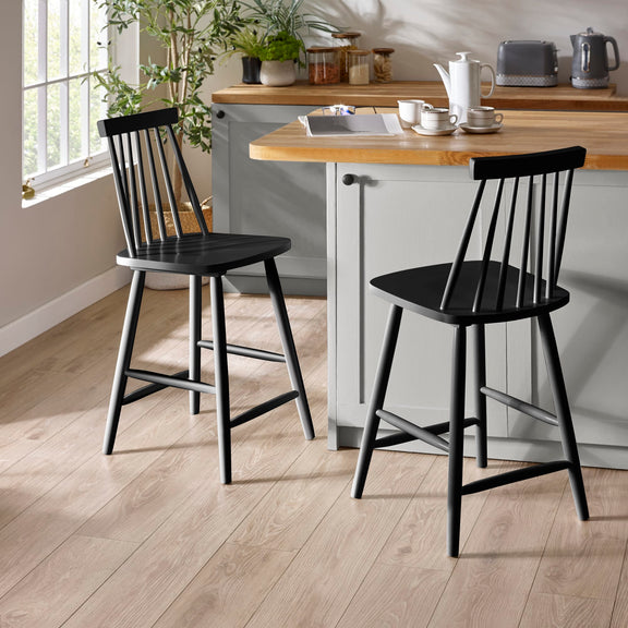Two black bar stools in front of a kitchen island with a wooden top.