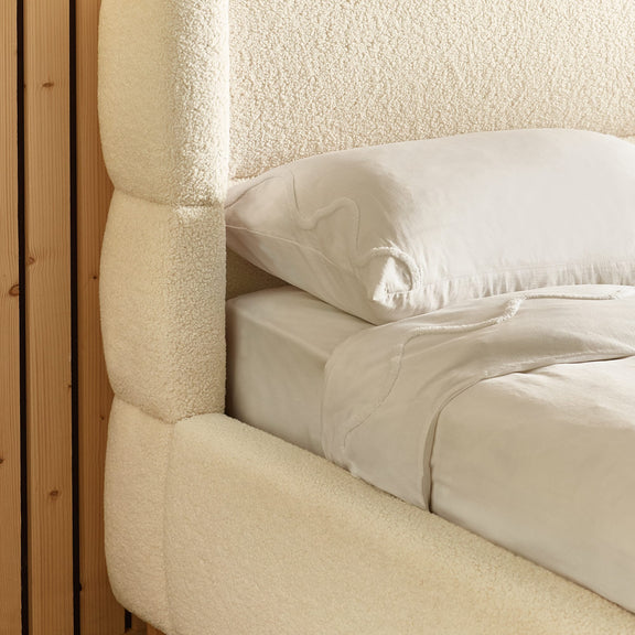Close-up of a textured headboard and bedding with a pillow.
