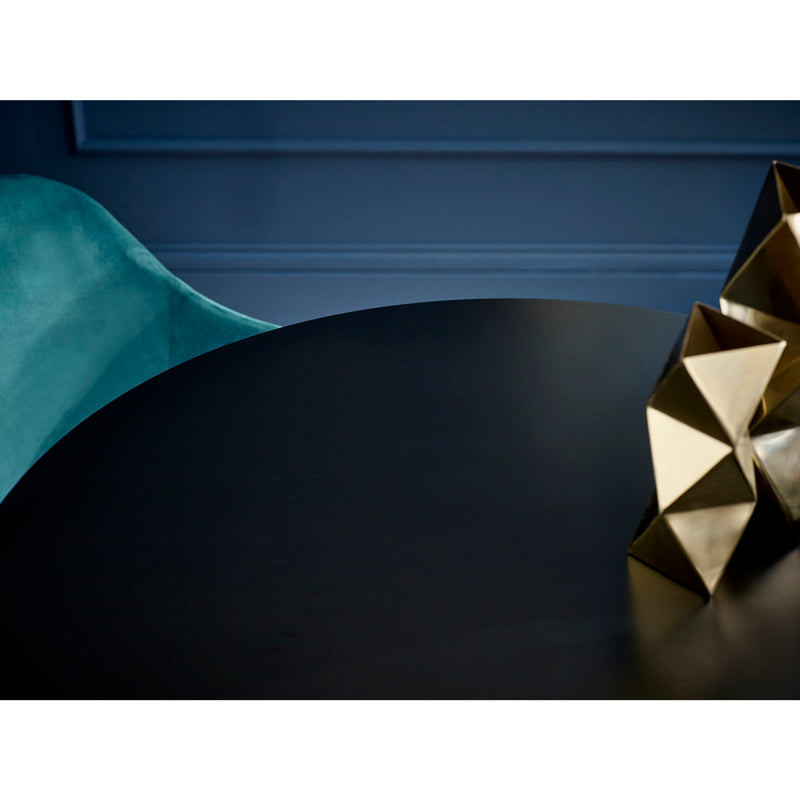 Gold geometric sculpture on a dark surface with a teal chair in the background