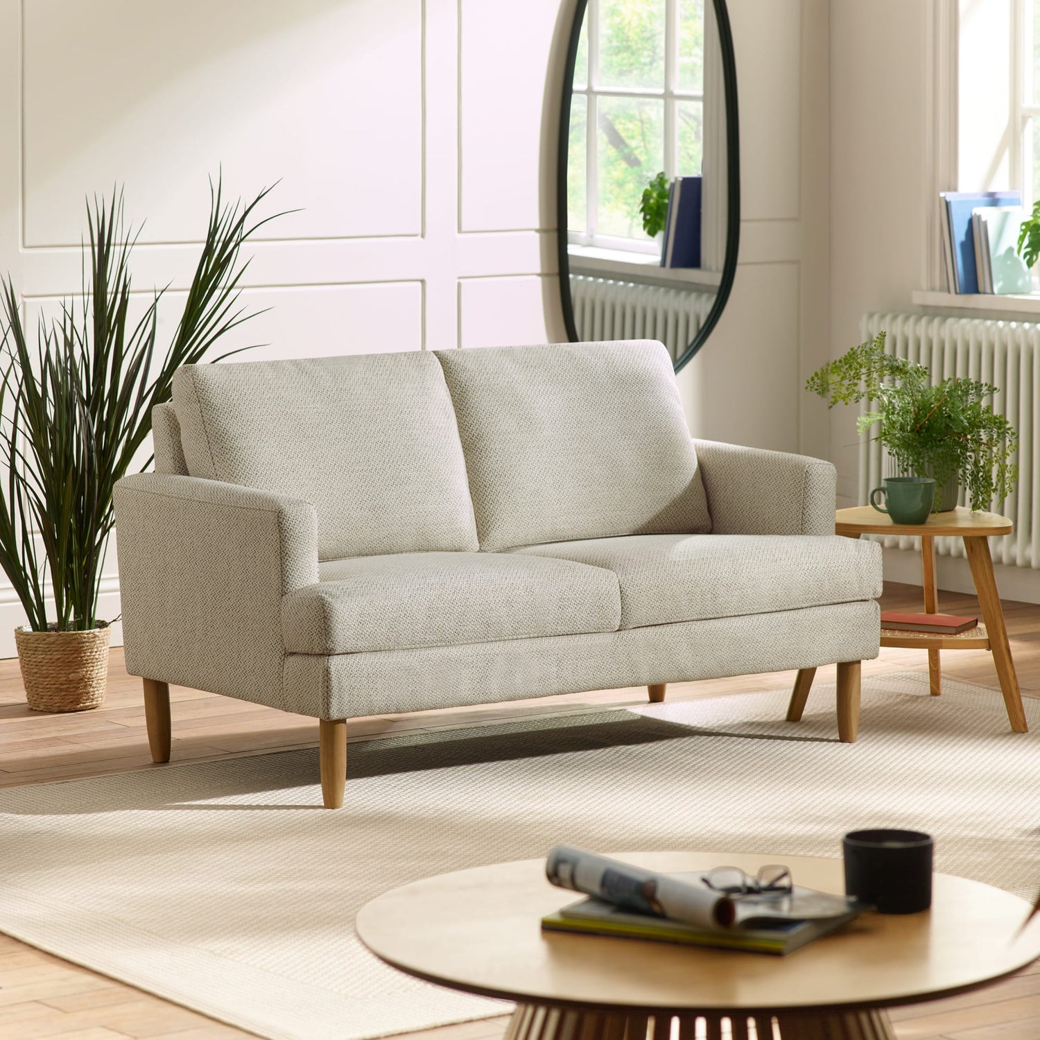 Light gray sofa in a living room with a round coffee table and plants.