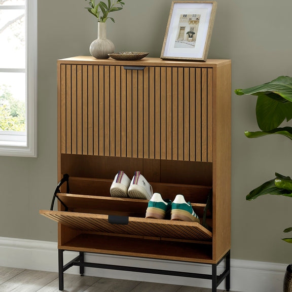 Wooden shoe cabinet with open door showing shoes, placed against a wall with decor items.