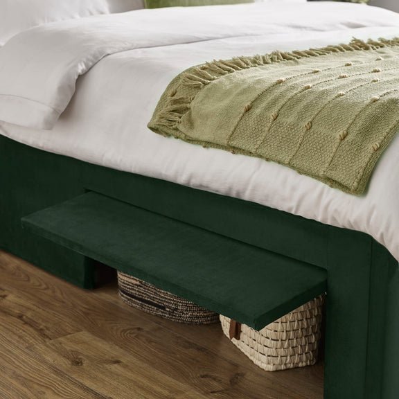 Green footstool next to a bed with white bedding and a green blanket.