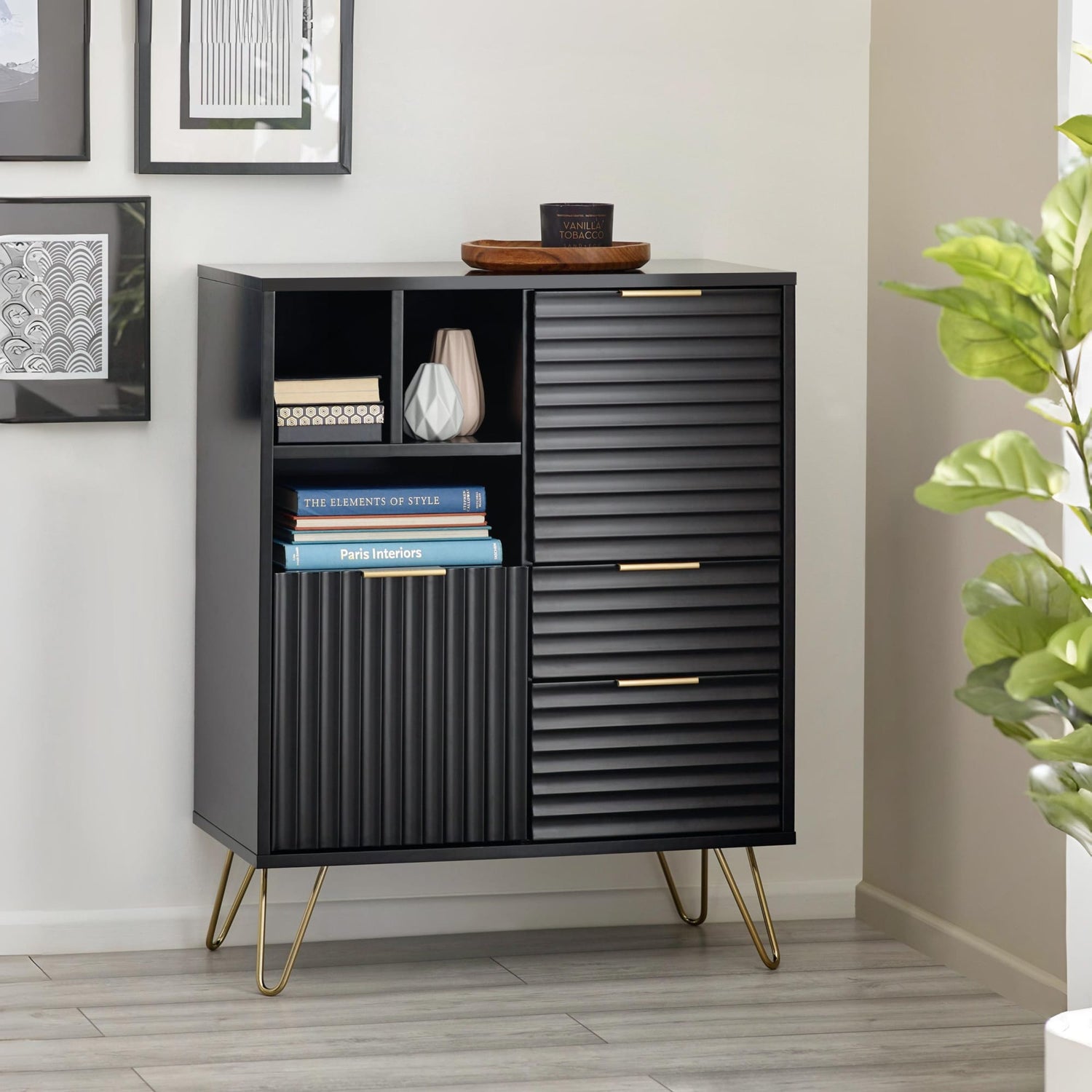 Black cabinet with gold legs in a room setting with books and decor items.