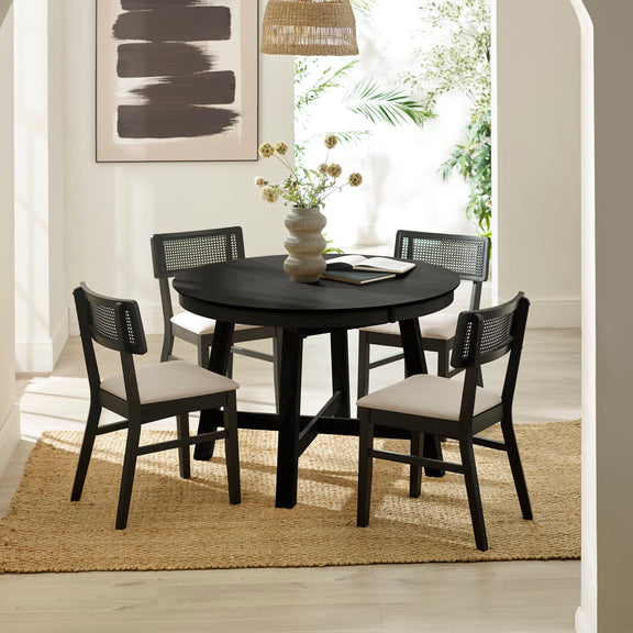 Black round dining table with four chairs in a room with a rug and decor.