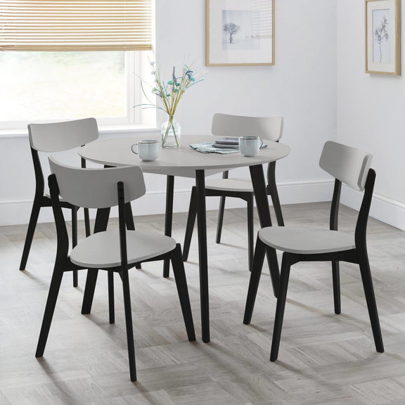 Round dining table with four chairs in a room with light wood flooring and white walls.