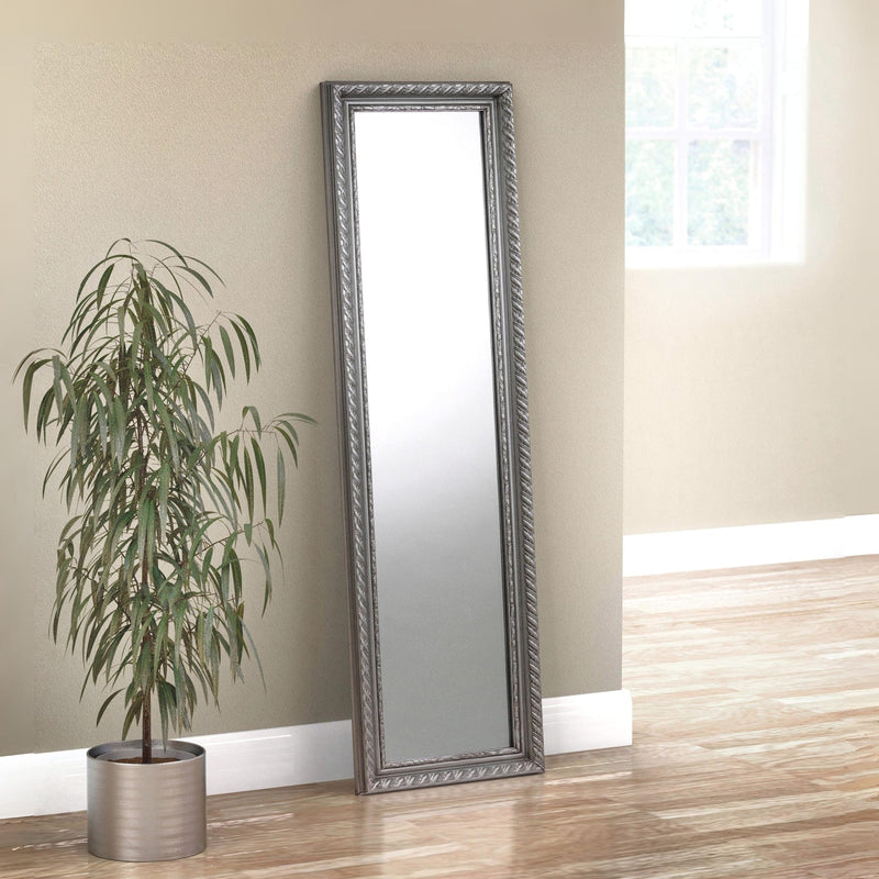 Silver framed mirror leaning against a beige wall next to a potted plant on a wooden floor.
