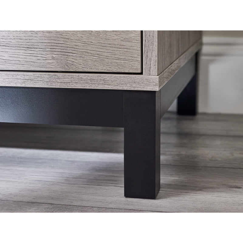 Close-up of a wooden drawer with a dark metal base on a wooden floor.