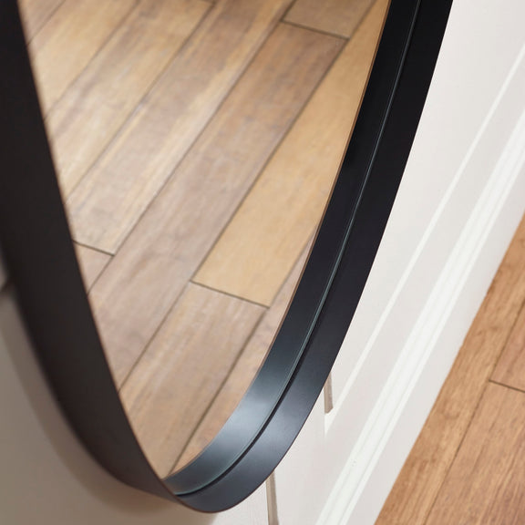 Round mirror with black frame on a wooden floor