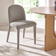 Gray upholstered chair next to a wooden table in a bright room with large windows.