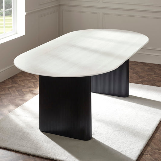Modern dining table with black base and white marble top in a room with wooden flooring and a window.