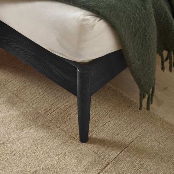 Close-up of a black wooden bed frame with a green blanket on a beige carpet.