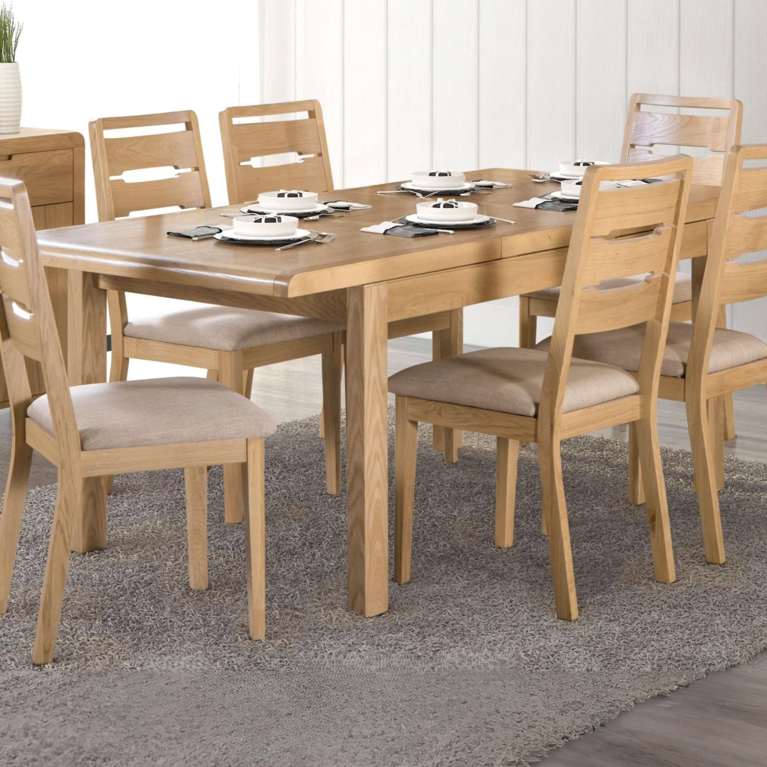 Wooden dining table set with chairs in a room with white walls and a rug.