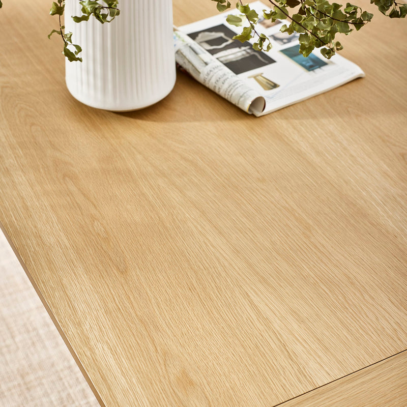 Close-up of a wooden floor with a vase, plant, and newspaper on a table.