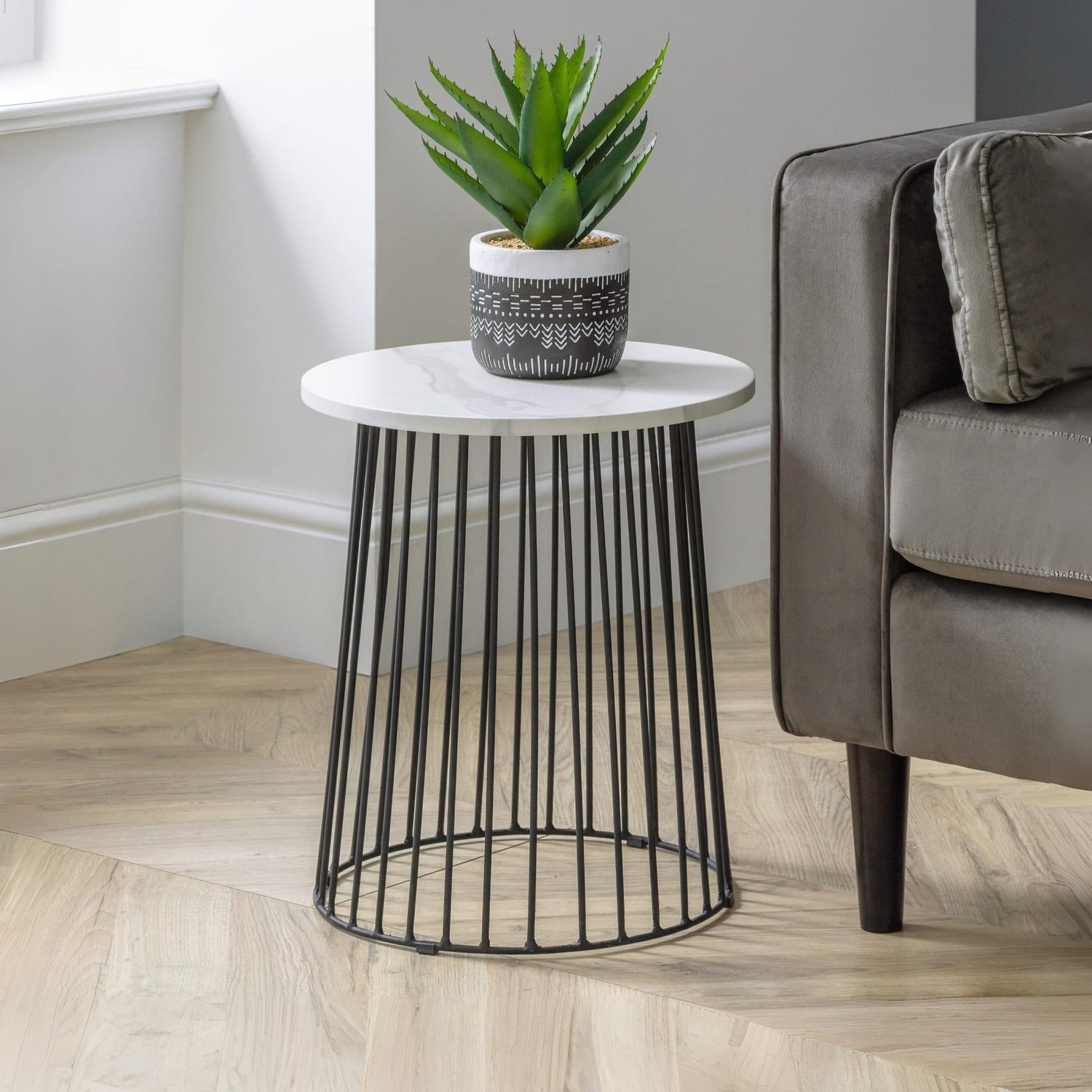 Small round side table with black metal base and white top next to a gray sofa in a living room.