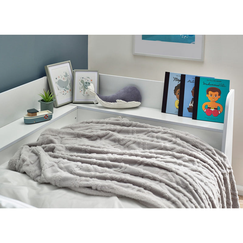 Gray blanket on a bed with a shelf above holding decorative items and books.