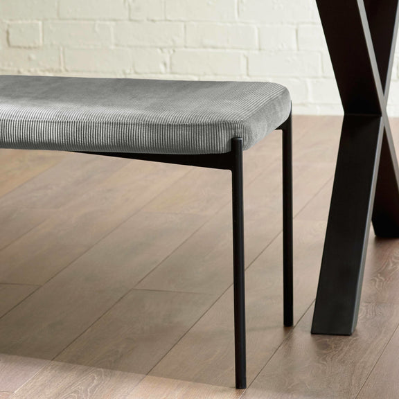 Gray upholstered bench with black legs on a wooden floor.
