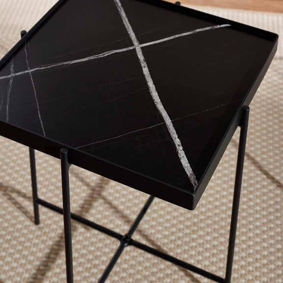 Black side table with a textured surface on a patterned carpet