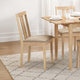 Wooden dining table with chairs on a patterned rug in a room with white walls.