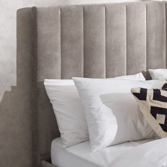 Gray upholstered headboard with white and patterned pillows against a light gray wall.