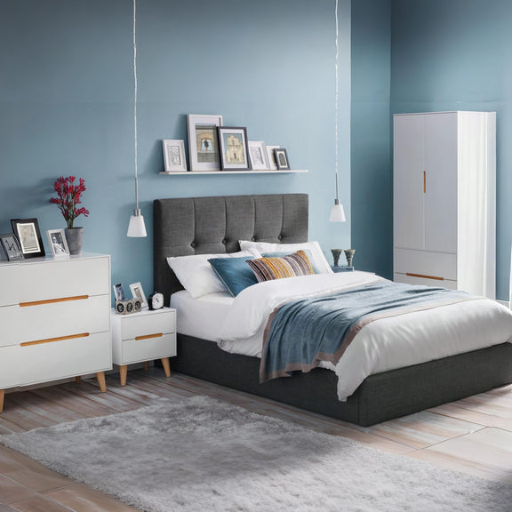 Modern bedroom with gray upholstered bed, white dresser, and blue walls.
