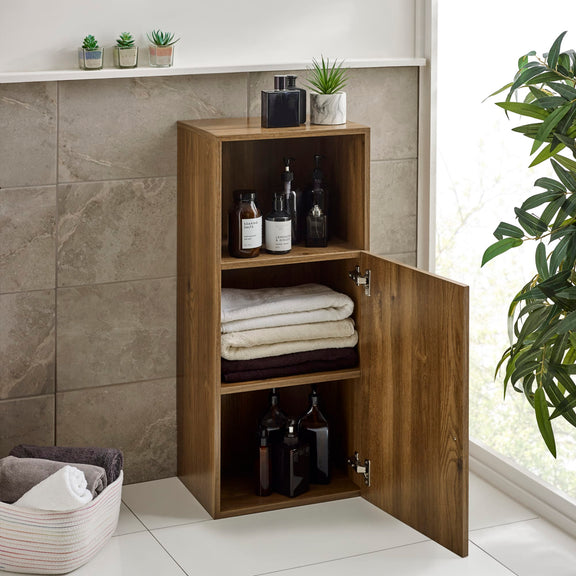 Wooden cabinet with open door displaying folded towels and bottles in a bathroom setting.