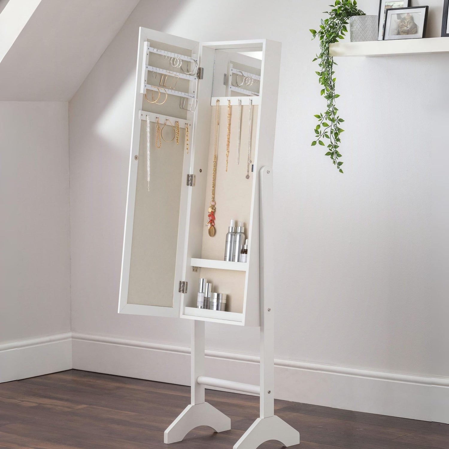 White standing mirror with jewelry storage in a room with a plant on a shelf.