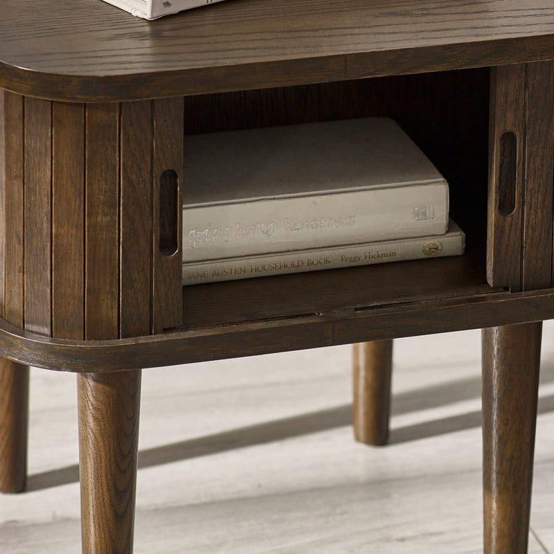 Wooden side table with a shelf holding books on a light wooden floor.
