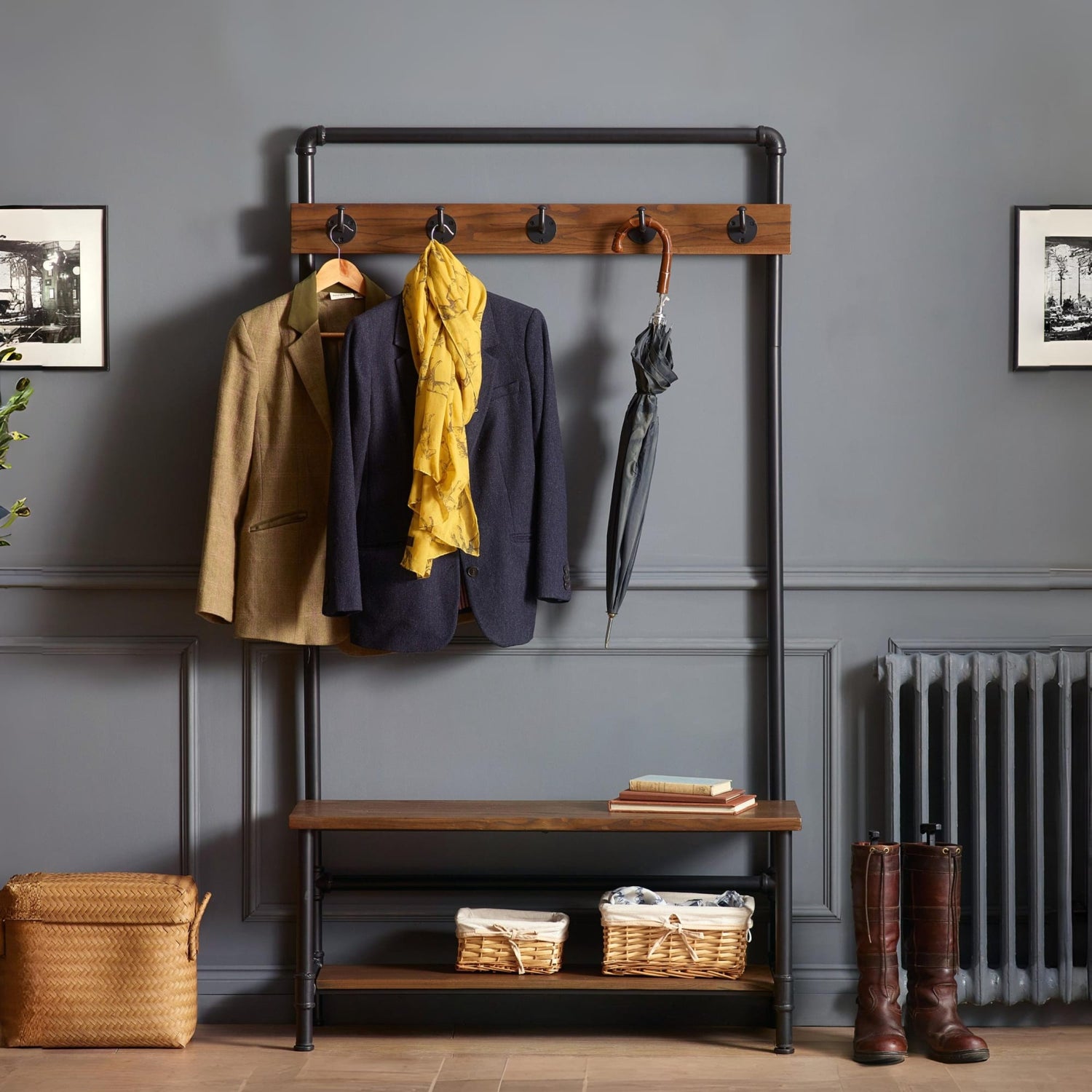 Coat rack with hooks holding coats and an umbrella against a gray wall.