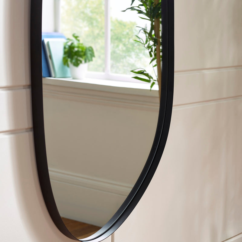 Round mirror with black frame on a white wall with a window in the background