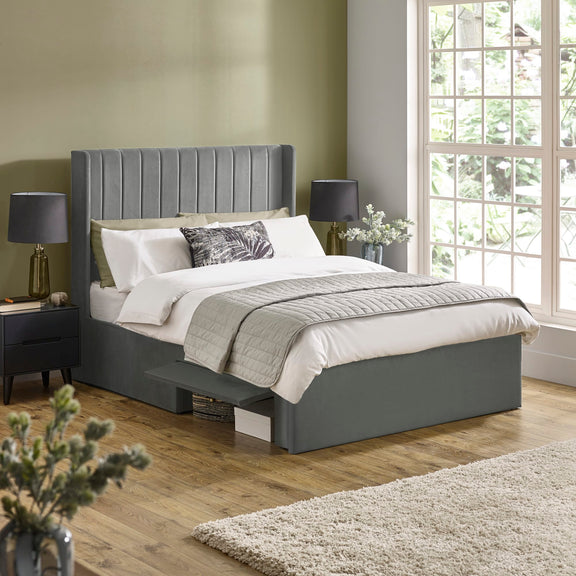 Gray upholstered bed in a bedroom with a large window and decorative elements.