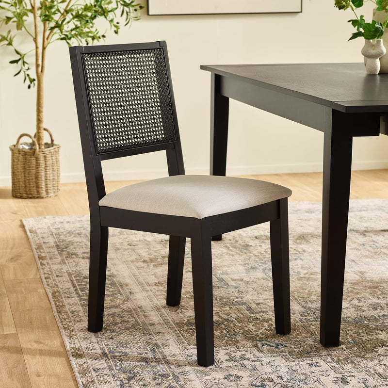 Black chair with woven backrest and beige cushion next to a wooden table in a room with a rug and plants.