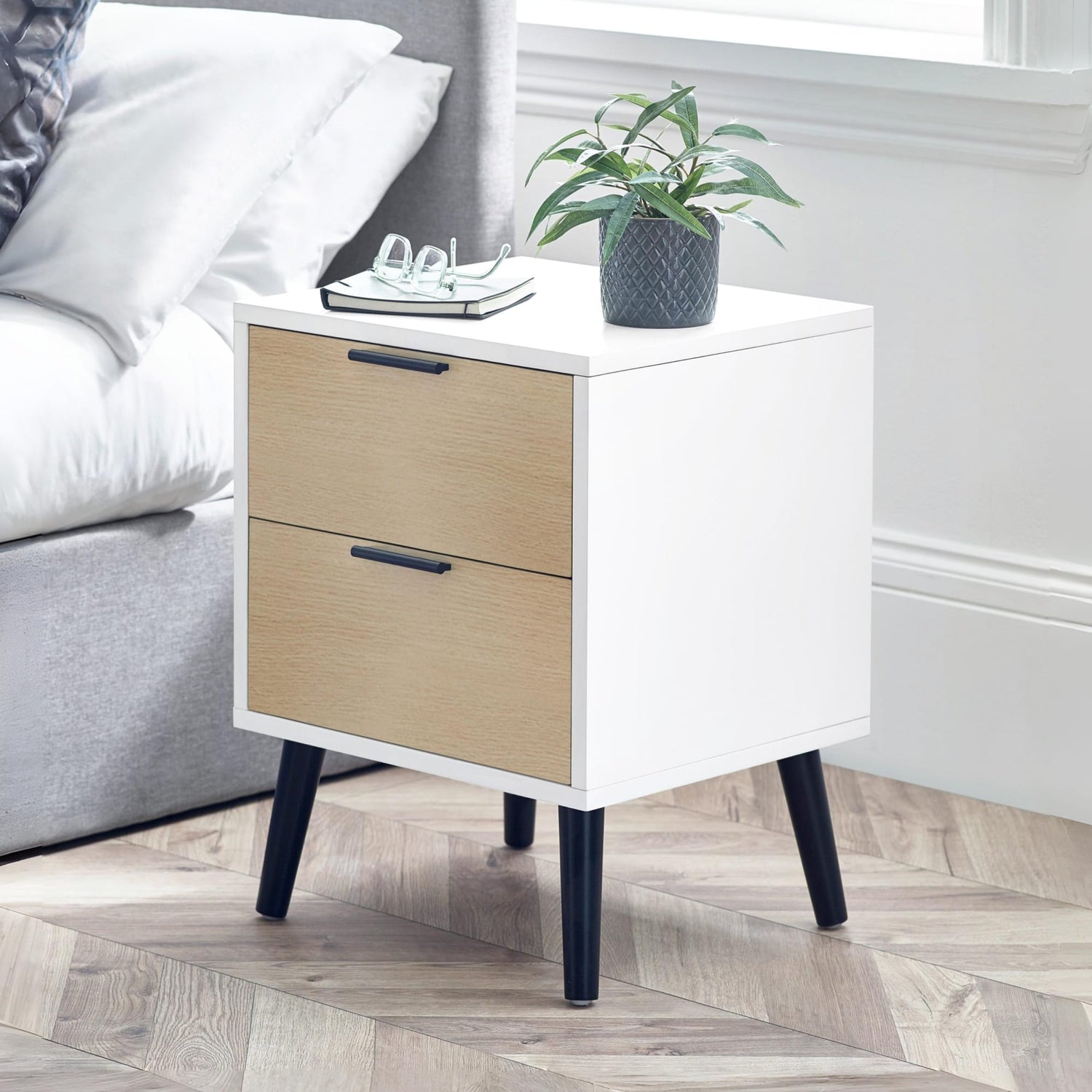 White nightstand with wooden drawers next to a bed in a bedroom.