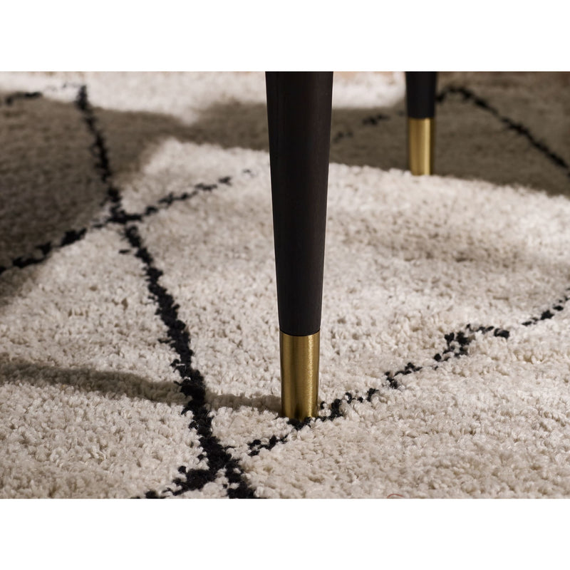 Close-up of a chair leg with black and gold finish on a textured beige carpet.