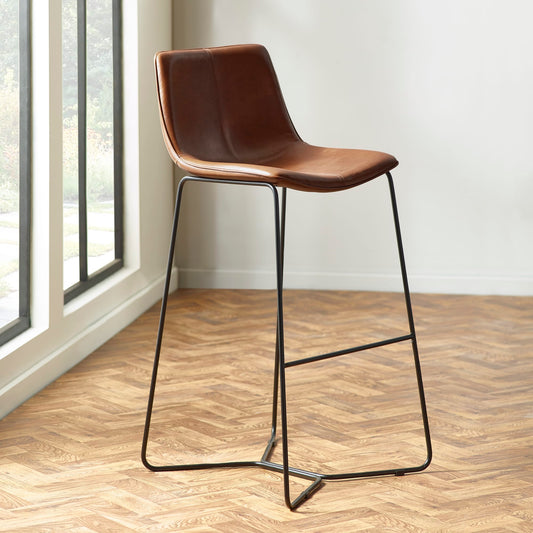 Brown bar stool with black metal legs on a wooden floor.