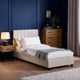 Neatly made bed with beige headboard in a bedroom setting.