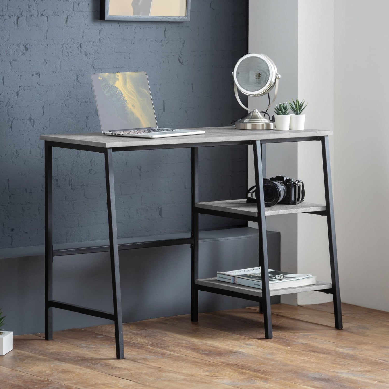 Modern desk with laptop, camera, and books against a gray wall.