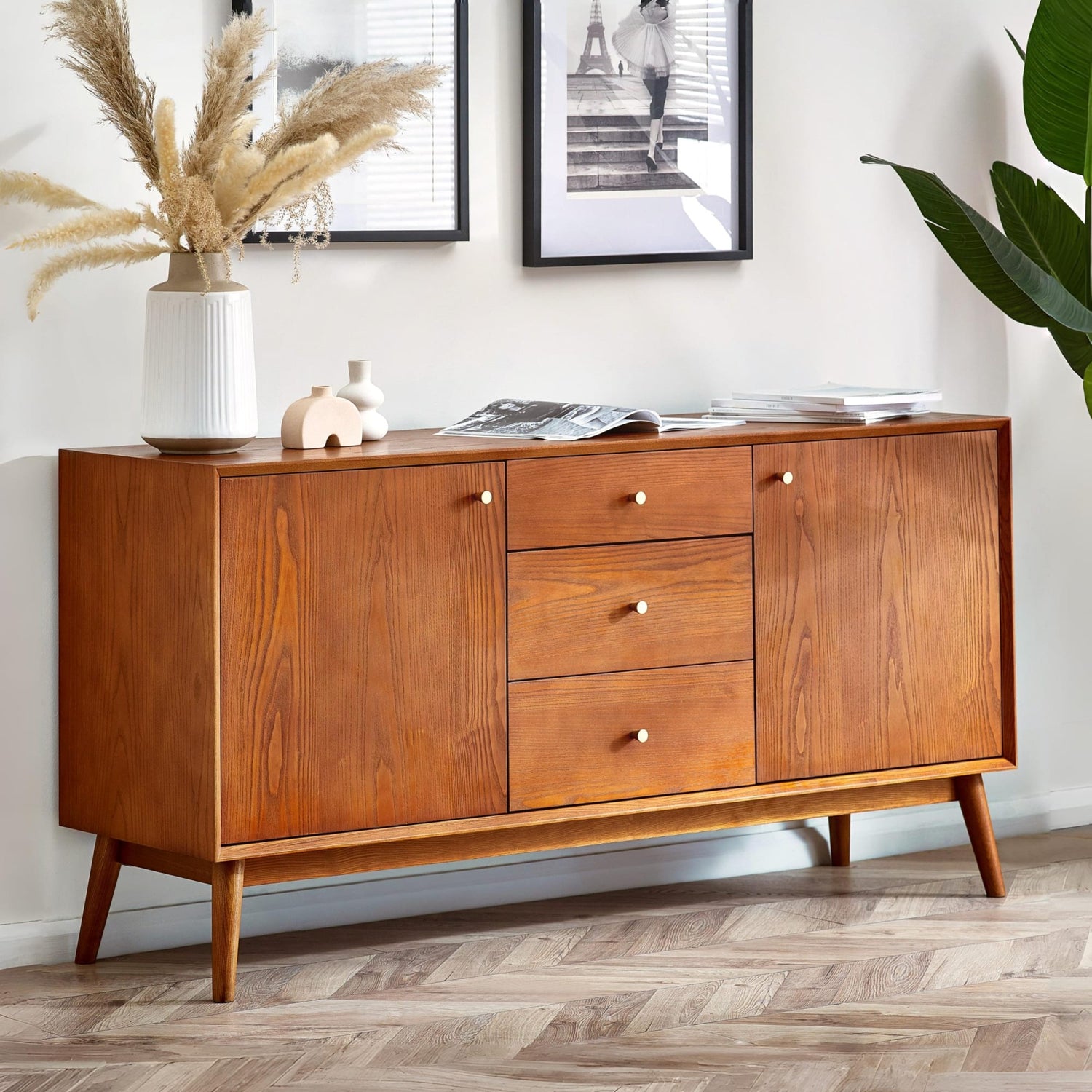 Wooden sideboard with decorative items in a room with framed pictures and plants.