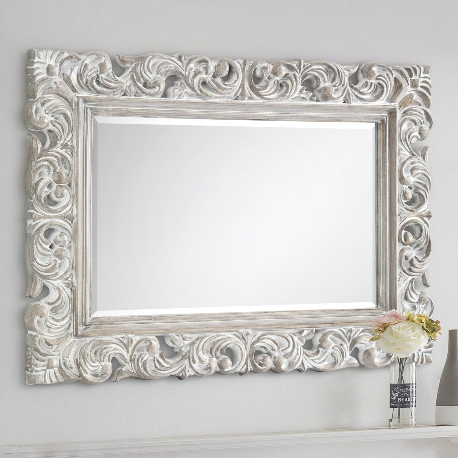 Decorative silver mirror with intricate patterns on a white wall.