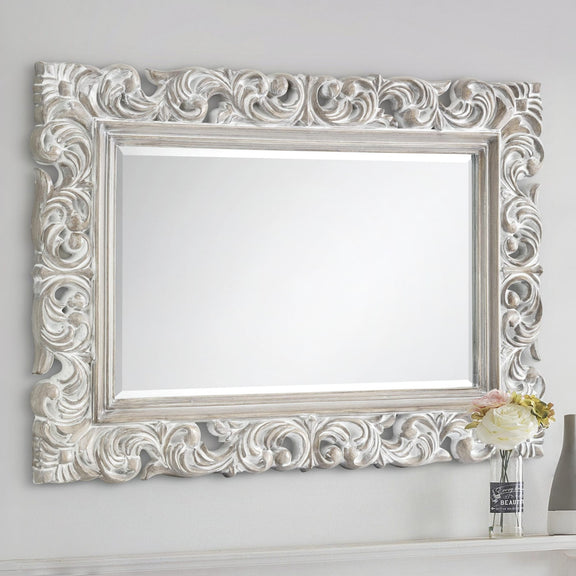 Decorative silver mirror with intricate patterns on a white wall.