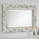 Decorative silver mirror with intricate patterns on a white wall.