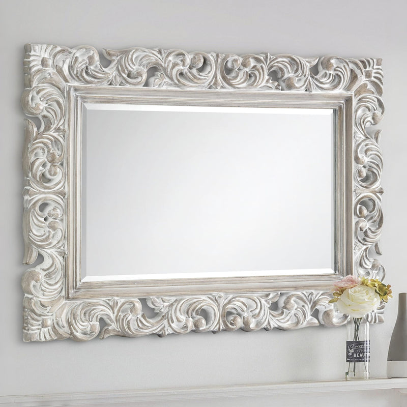 Decorative silver mirror with intricate patterns on a white wall.