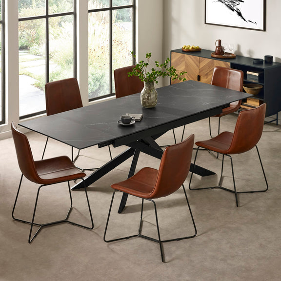 Dining table with brown chairs in a modern room with large windows.