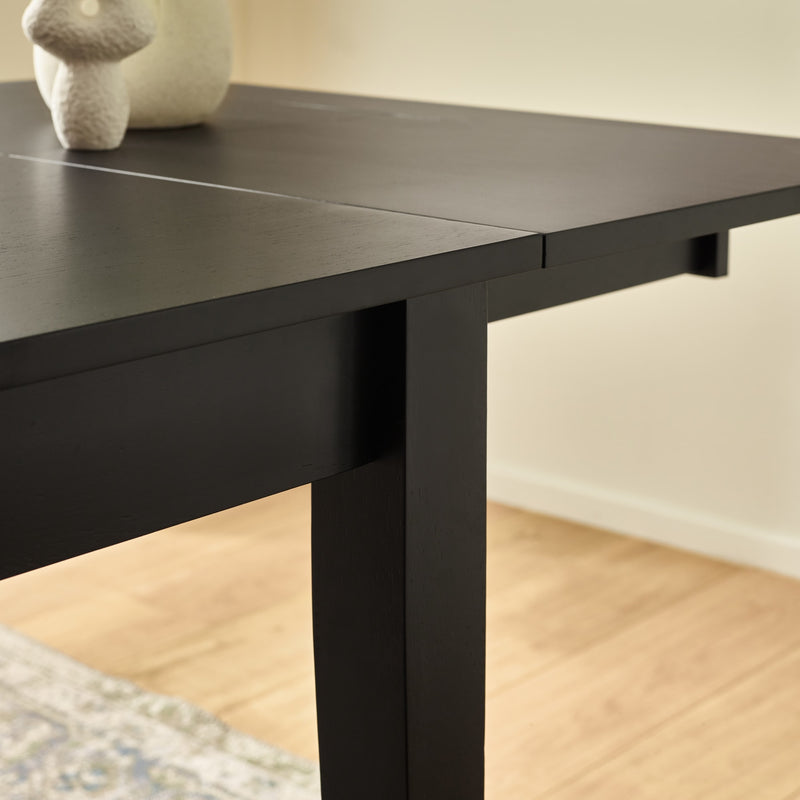 Black dining table with a white vase on a wooden floor.